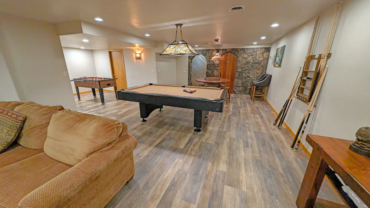 This image features a recreation room with a pool table, sofa, foosball table, stone wall, and bar stools. The space is designed for socializing and friendly competition, with ample room for team members to gather, relax, or engage in games.