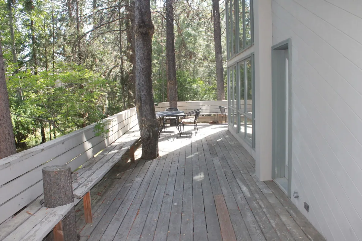 A spacious wooden deck surrounded by towering pines, featuring comfortable outdoor seating and a dining area. The tranquil scene hints at the possibilities for al fresco meals, relaxation, and social gatherings amid nature.