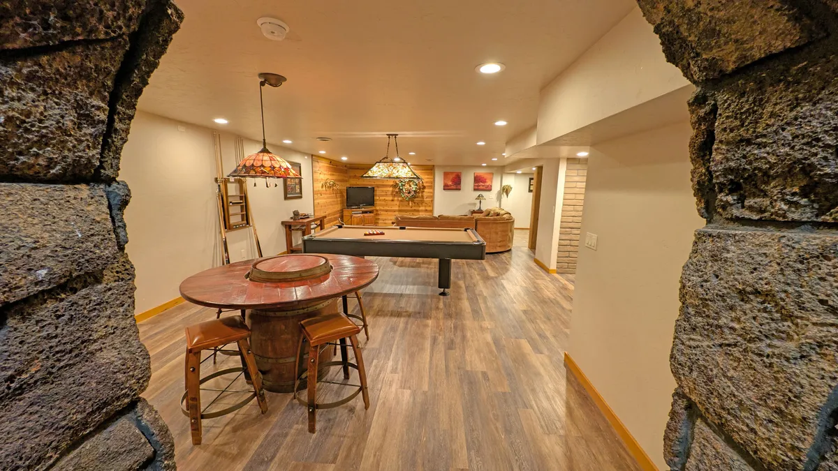 A welcoming recreation area with a pool table, round table for dining or meetings, comfortable seating, decorative lighting, and a stone archway that gives the space character. The room is ideal for informal meetings, brainstorming, and socializing.