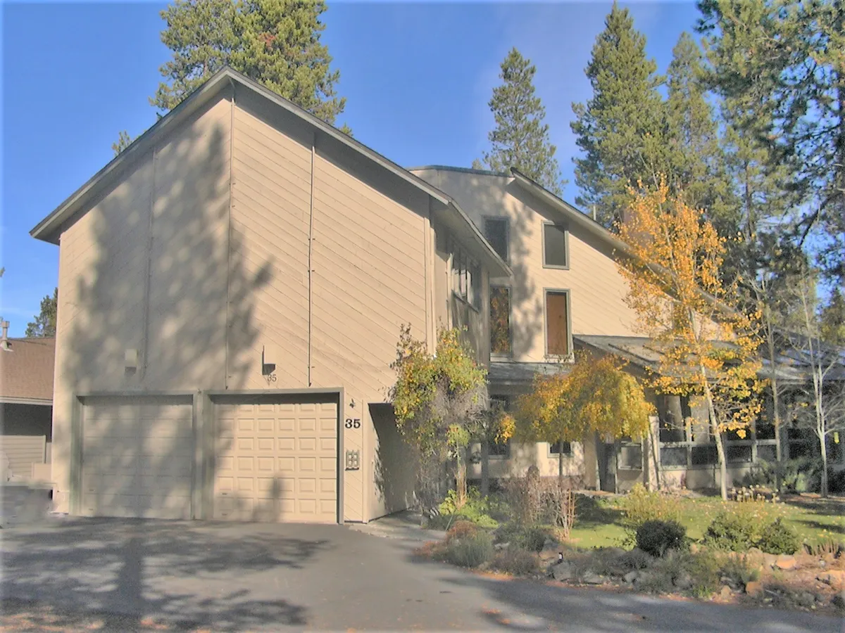 The inviting front exterior of the home, framed by tall trees and vibrant foliage, presents a sense of welcome and connection to the outdoors. The garage and walkways suggest easy access to gear or bikes and reinforce the property as a launching pad for Sunriver adventures.