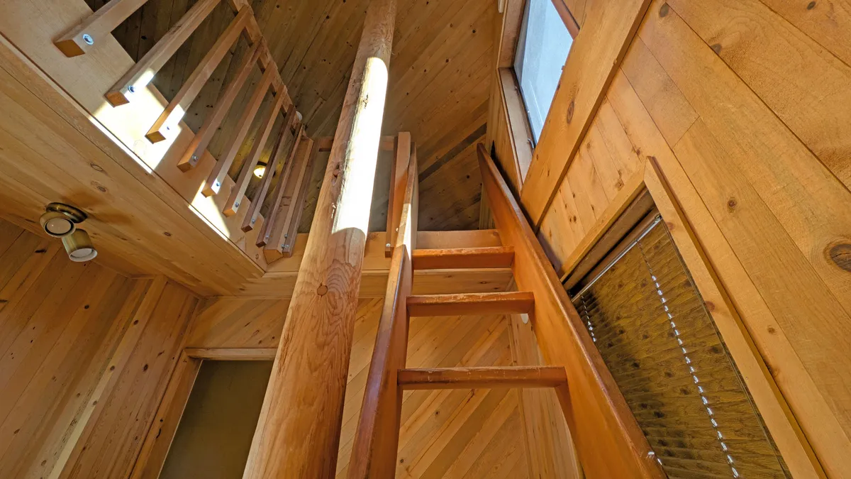 A view of a wooden staircase leading up to a bright loft area, with exposed beams and natural light pouring in through large windows. The space feels cozy and secluded—perfect for breakout sessions or a quiet place to recharge.