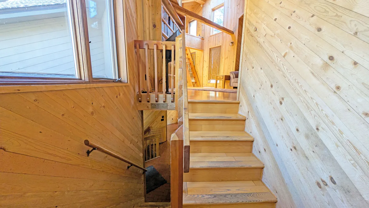 A view from inside the home showcasing a staircase, wood paneling, and large windows that let in ample natural light. The windows frame views of the outdoors, suggesting proximity to the surrounding natural environment and easy access to adventure.