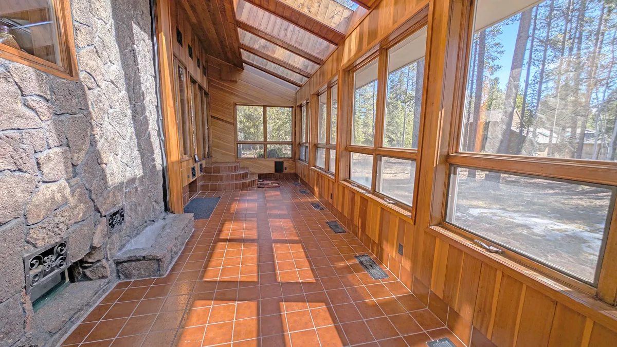 A sun-filled room with wooden paneling, large windows, a stone wall, and terracotta tiles. The space exudes tranquility, with sunlight streaming in, perfect for relaxation or enjoying nature views from the indoors.