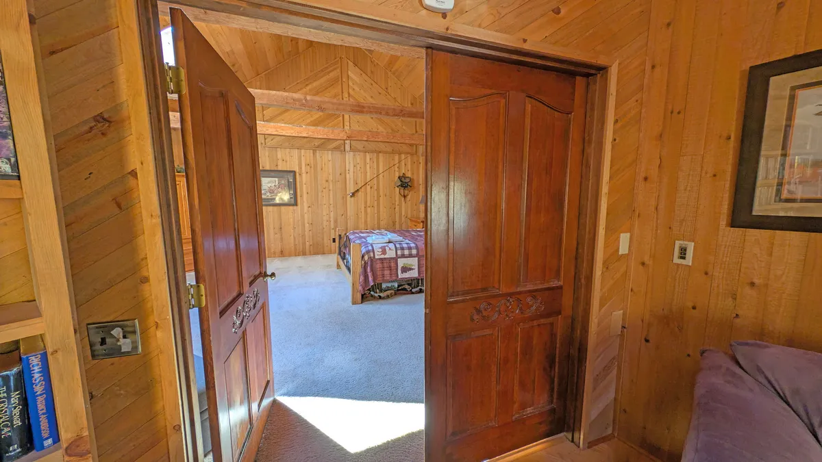 A serene king suite with wooden double doors, a beautifully quilted bedspread, and wood-paneled walls. The room is designed for relaxation and privacy, offering a peaceful retreat for guests seeking spacious comfort on the main level.