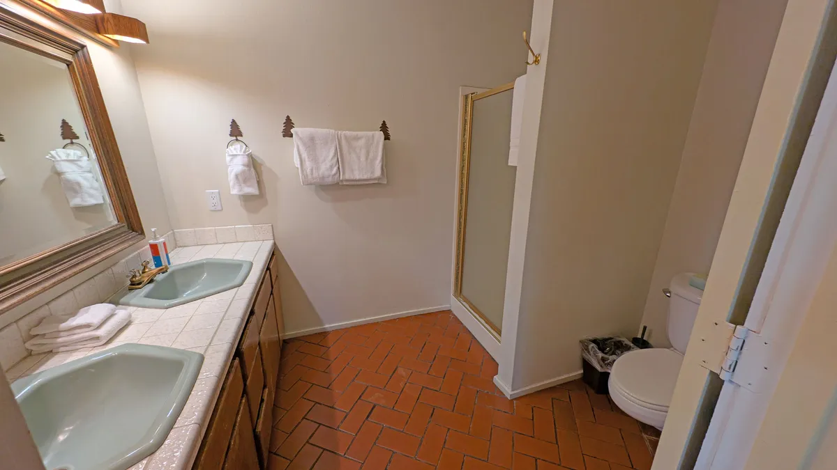 This bathroom image features a double sink with mirrors, a shower stall, toilet, and fresh towels, all in a clean, modern setting. The overall feel is calm and functional, reinforcing the comfort and convenience available on the entertainment level.